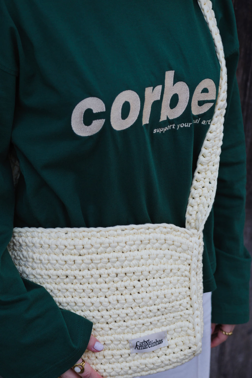 Yellow cream crochet crossbody bag with a wide strap, styled with a dark green streetwear long-sleeve with embroidered Corbet logo