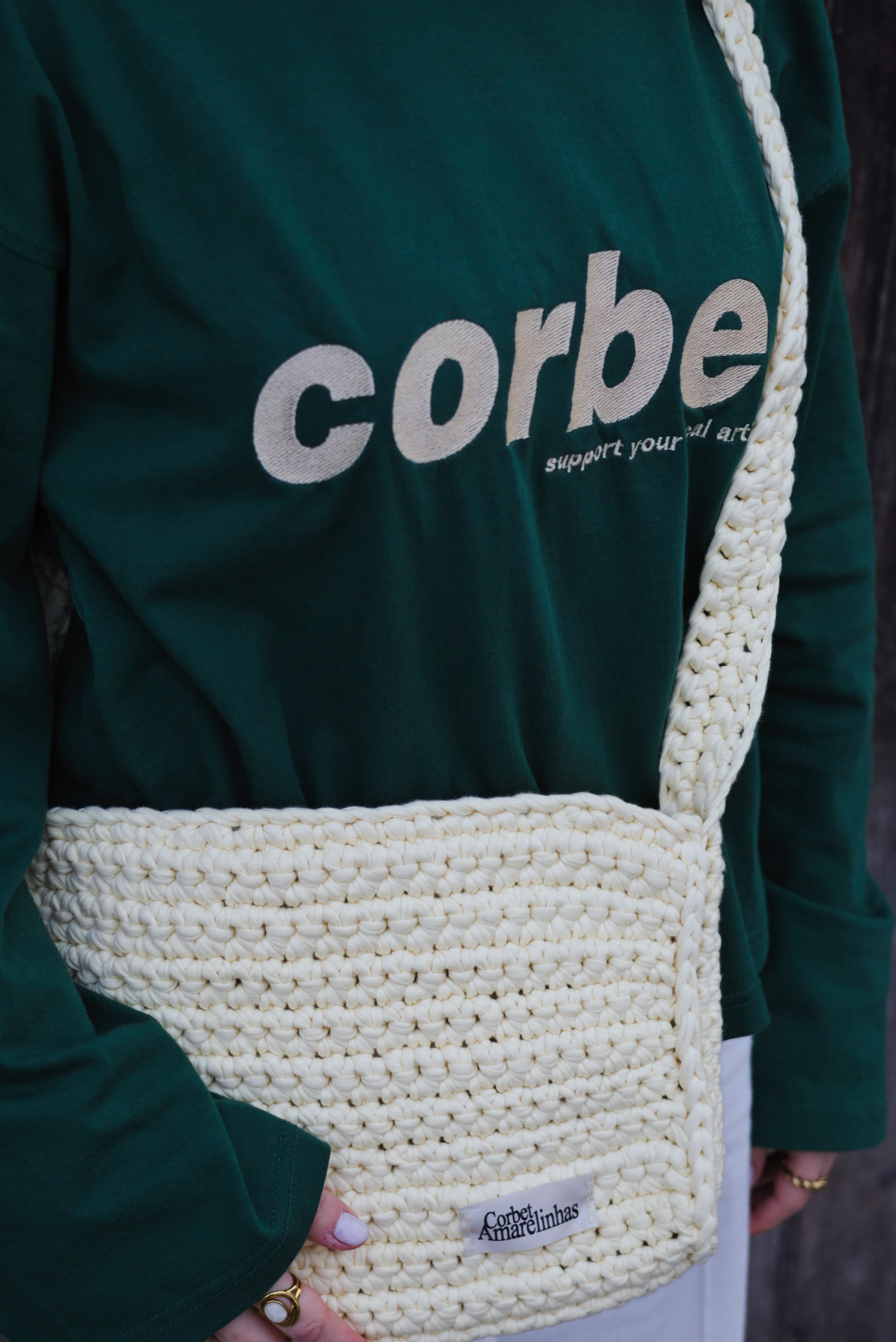 Yellow cream crochet crossbody bag with a wide strap, styled with a dark green streetwear long-sleeve with embroidered Corbet logo