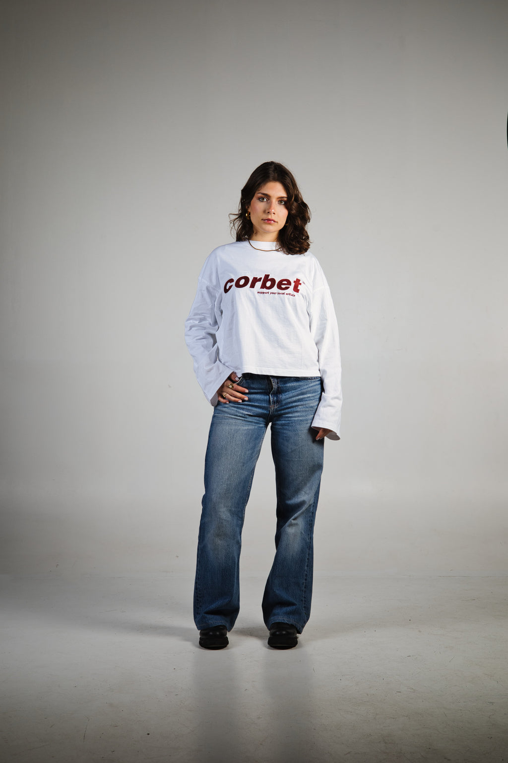 Person wearing a white sweatshirt with 'Corbet' embroidered logo and blue jeans on a gray background