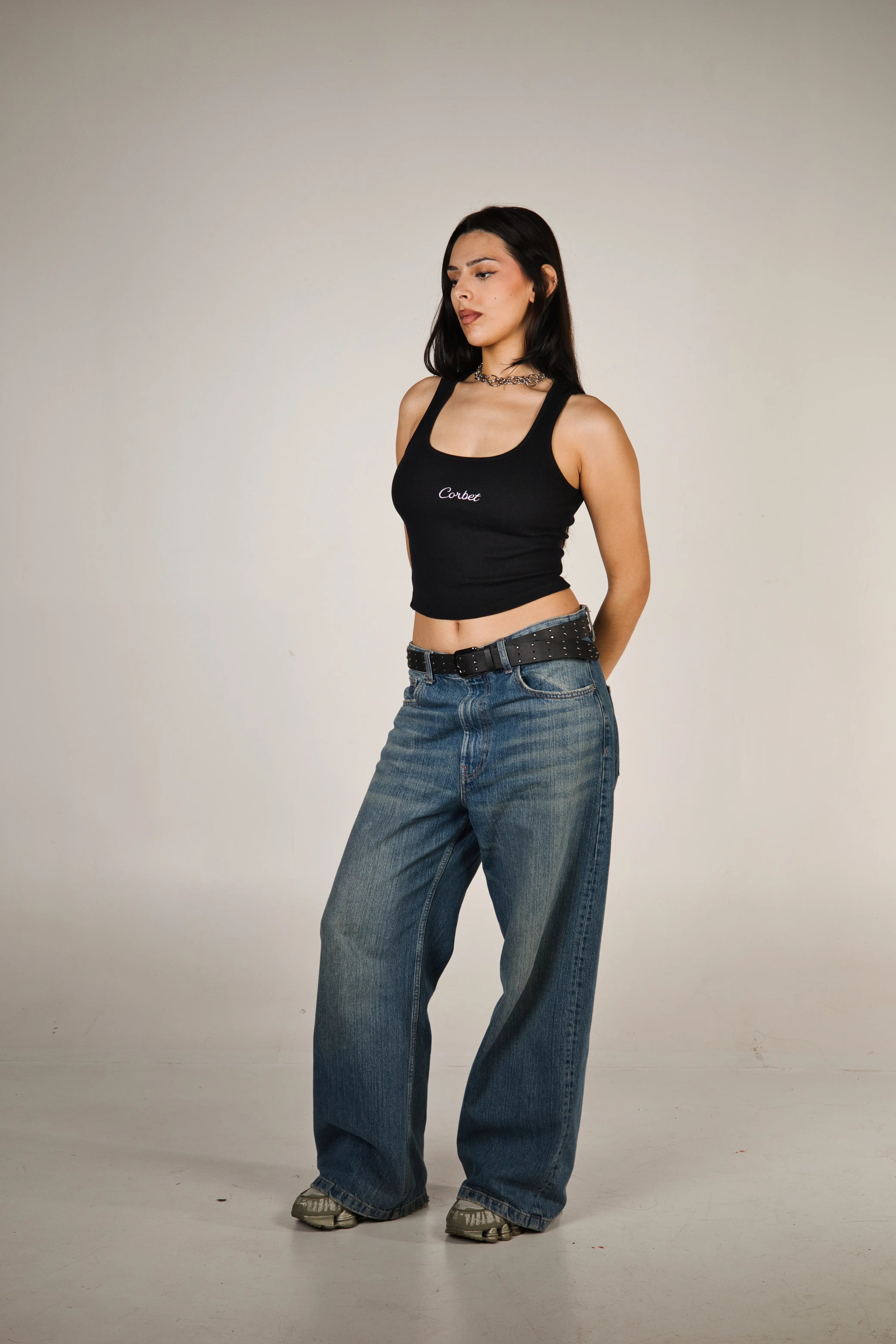 Woman wearing a black tank top with 'Corbet' text and blue jeans on a plain background