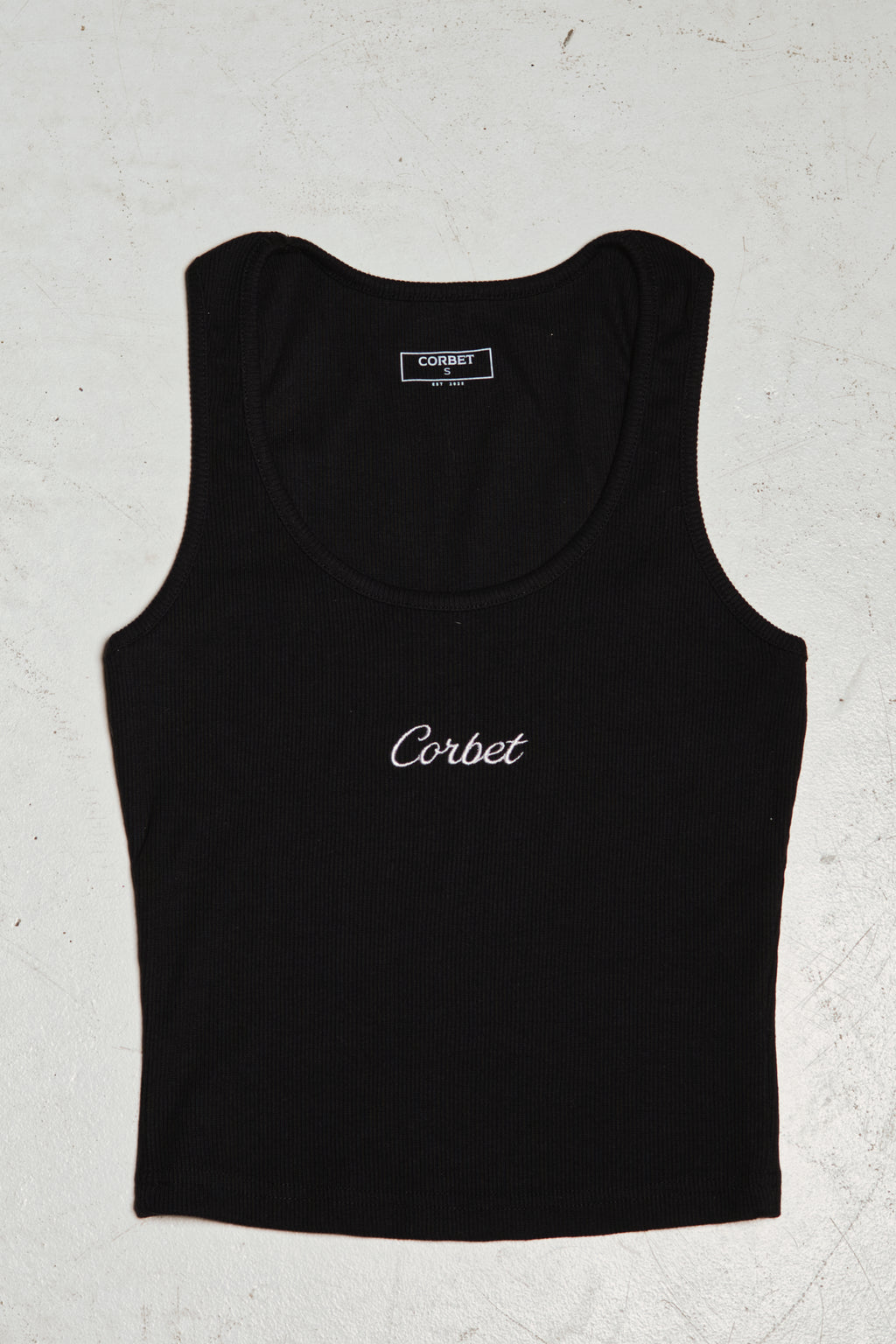Black tank top with embroidered 'Corbet' branding on a textured white background