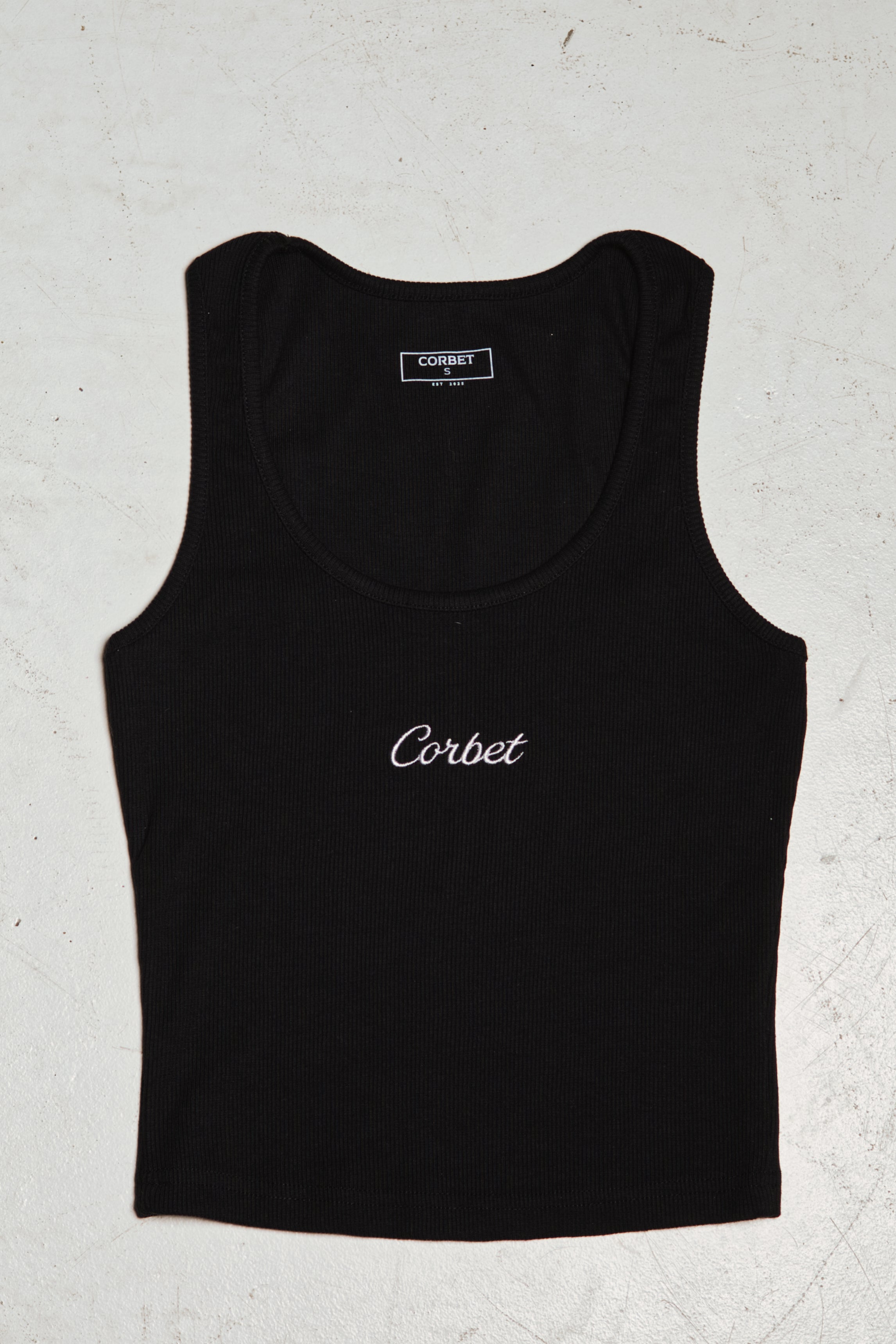 Black tank top with embroidered 'Corbet' branding on a textured white background
