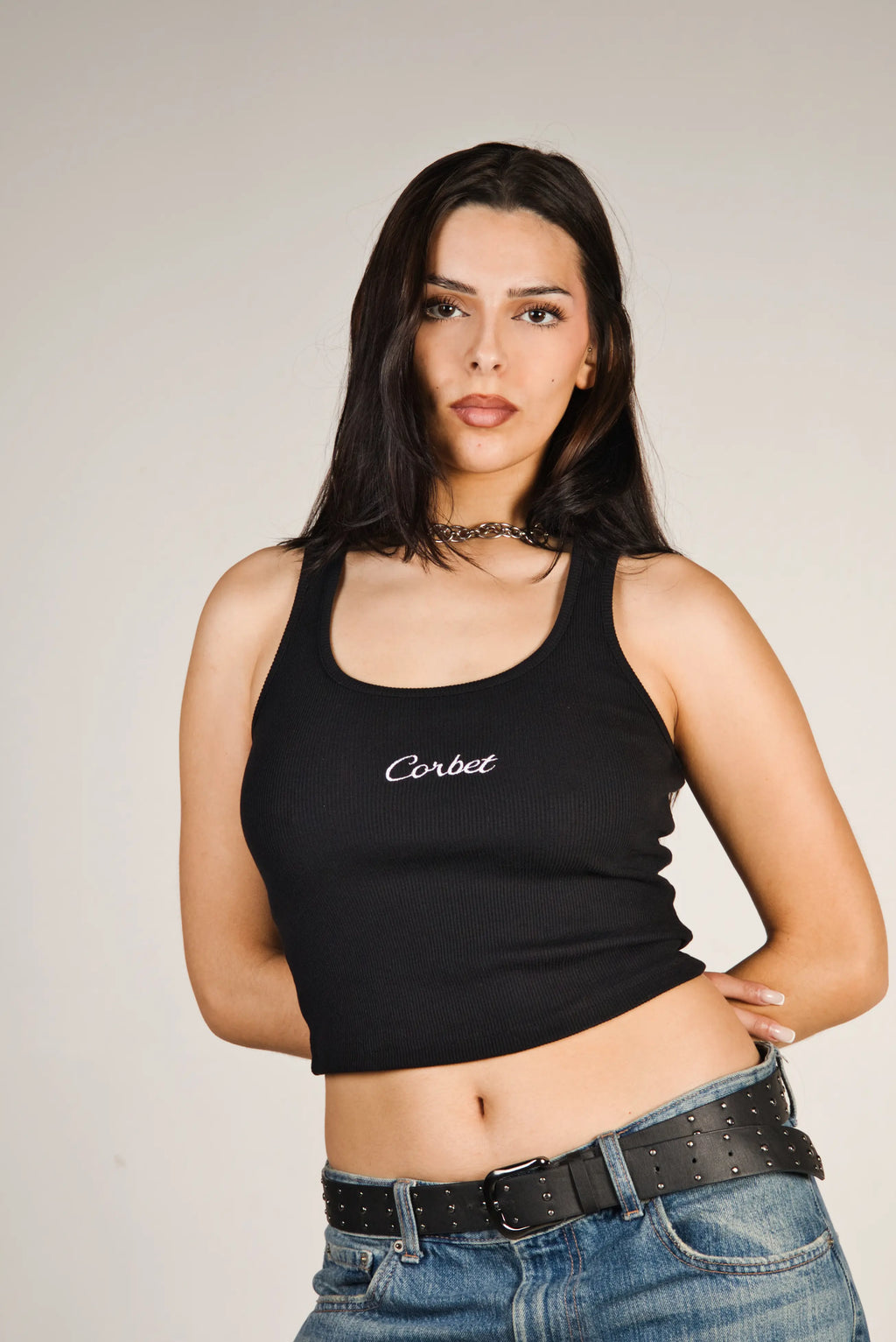 Woman wearing a black tank top with 'Corbet' text and blue jeans on a plain background