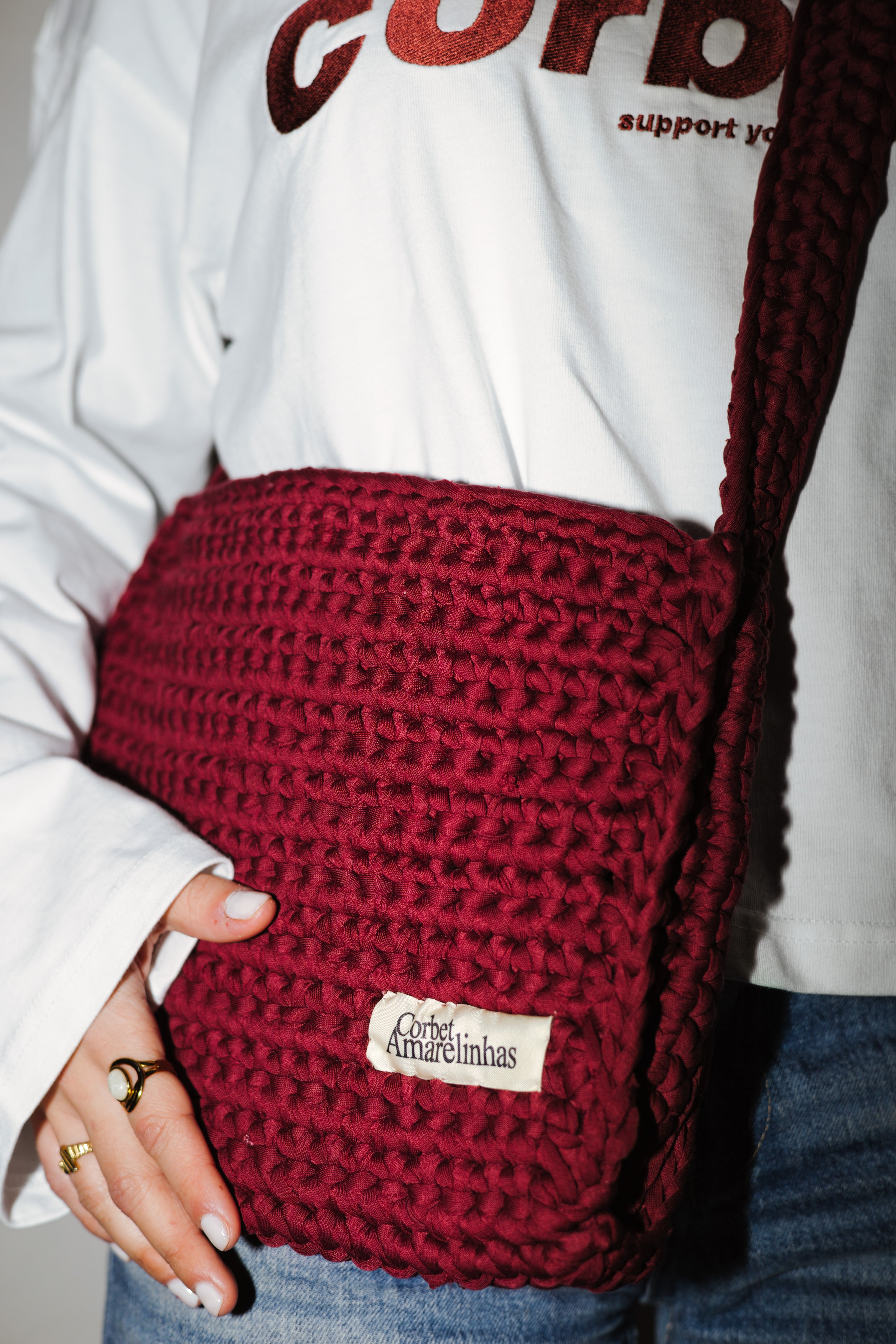 Red knitted bag with a brand label held by a person wearing a white sweatshirt.
