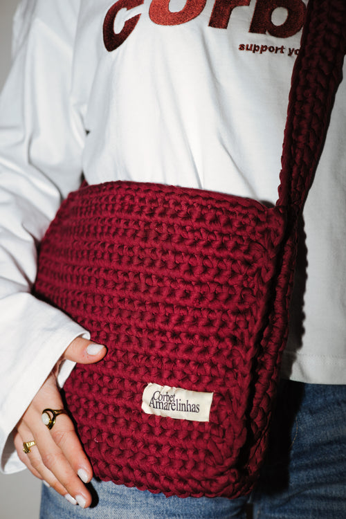 Red knitted bag with a brand label held by a person wearing a white sweatshirt.