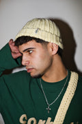 Person wearing a green long sleeve and yellow knitted beanie with the label "Corbet x Amarelinhas"