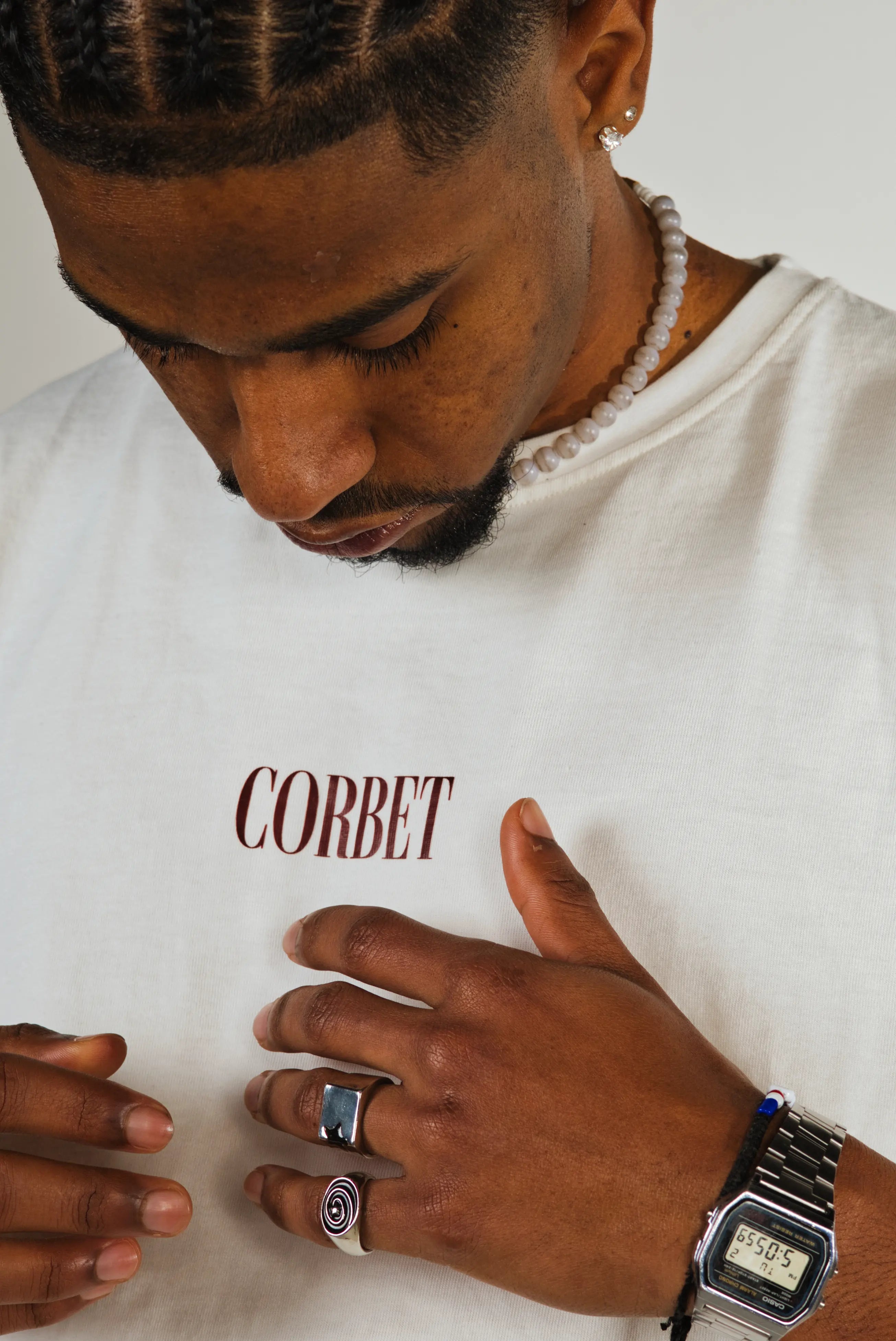 Man wearing a white t-shirt with 'CORBET' text, looking down at his hands.