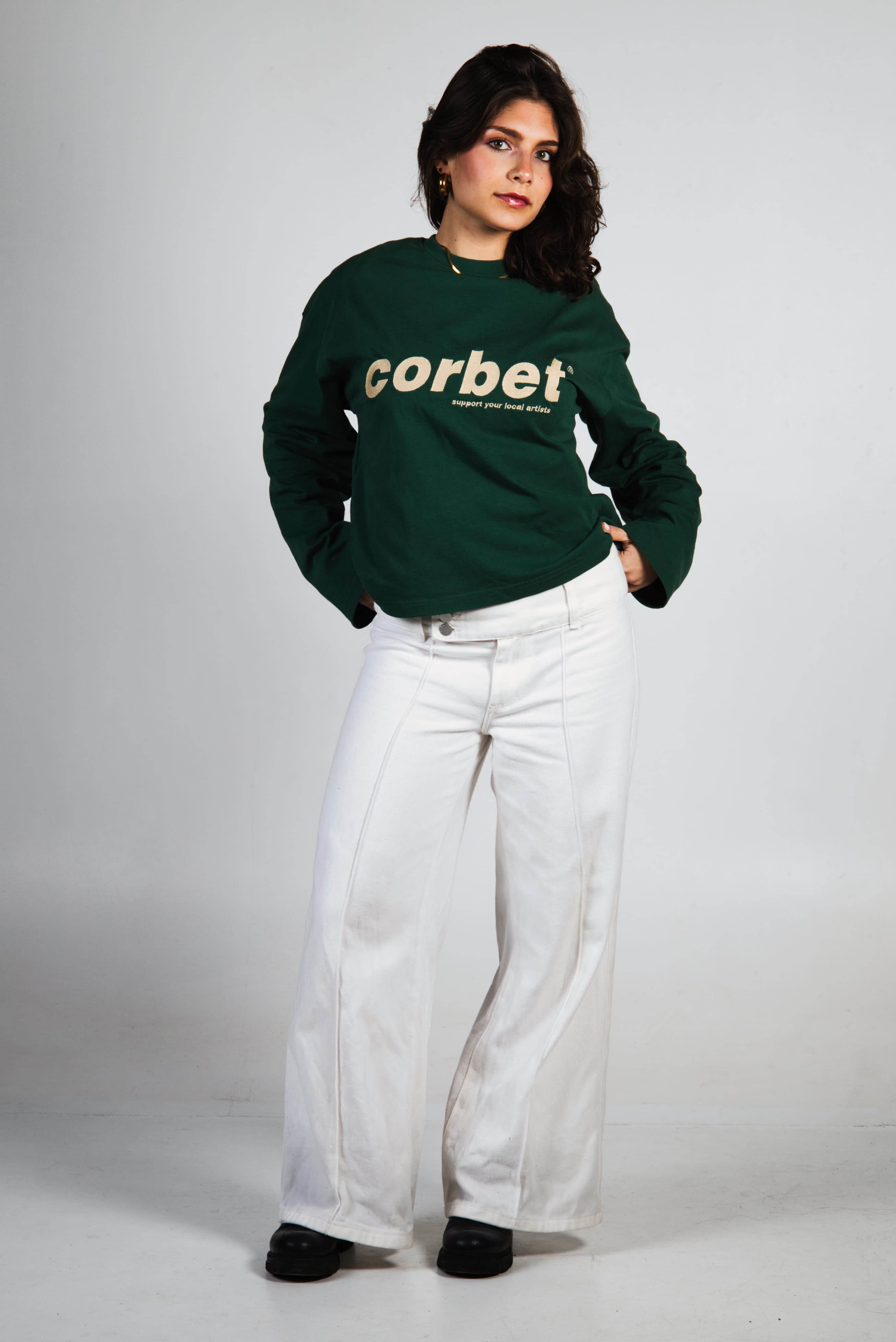 Woman wearing a green long sleeve with 'corbet' embroidered logo 