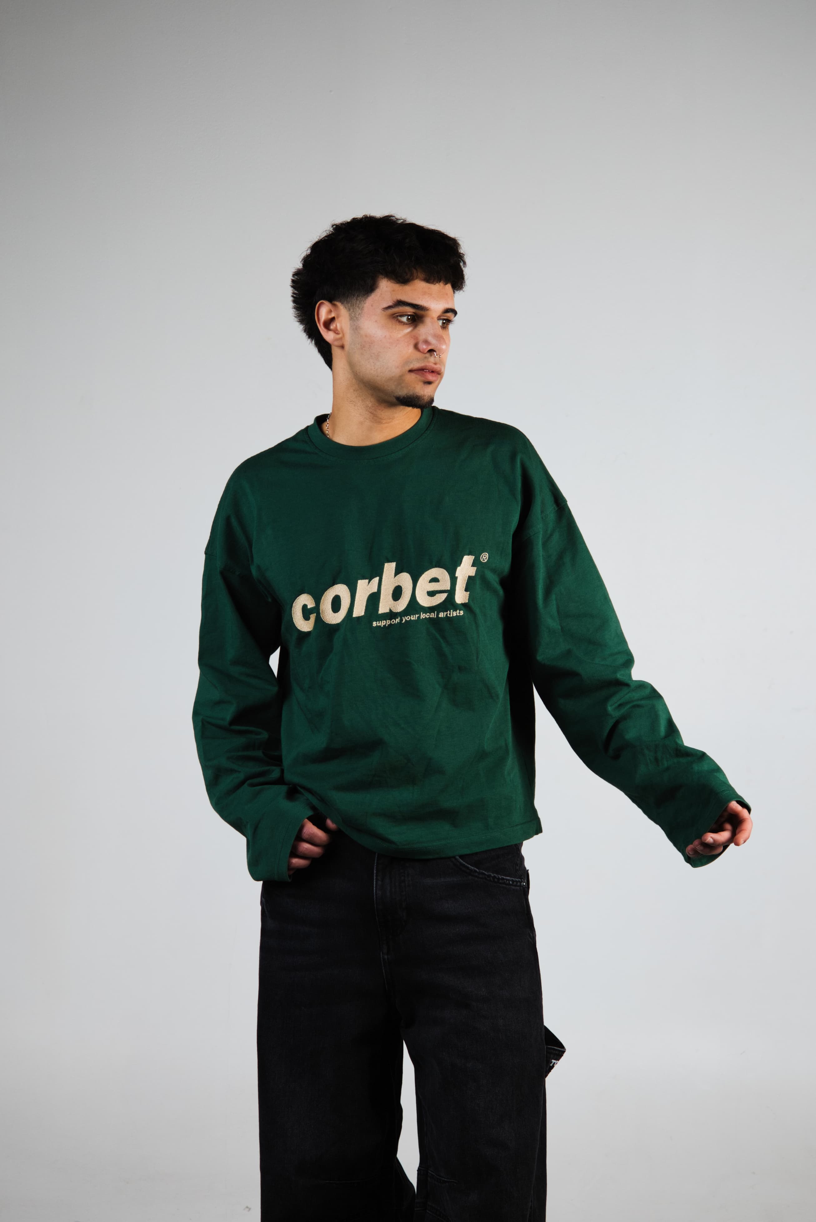 Man wearing a green long sleeve with 'corbet' embroidered logo on a plain background