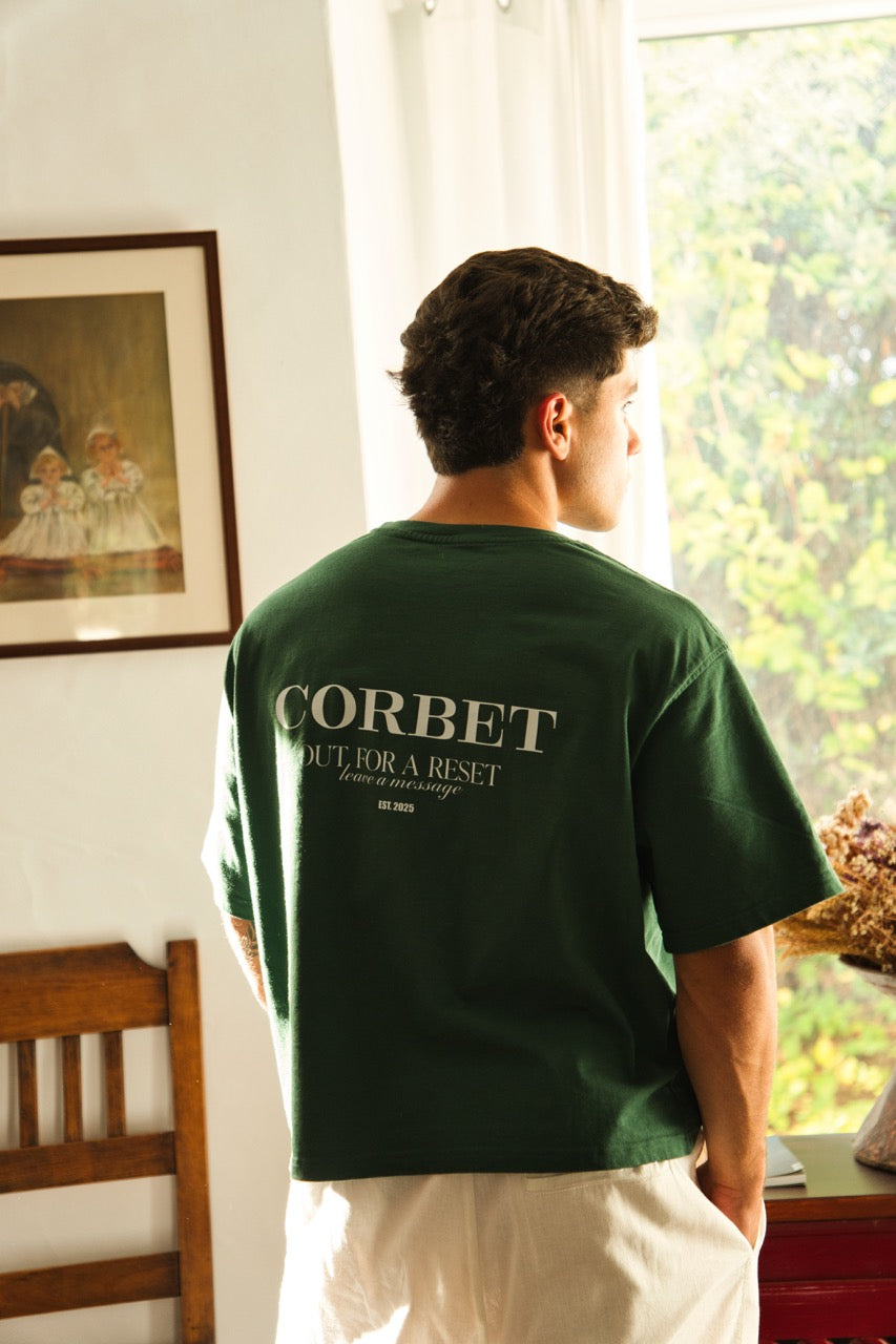 Person wearing a green t-shirt with 'Corbet' text, standing in a room with a painting and window.
