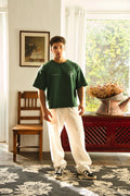 Man wearing a green t-shirt and white pants standing in a room with a window and furniture.
