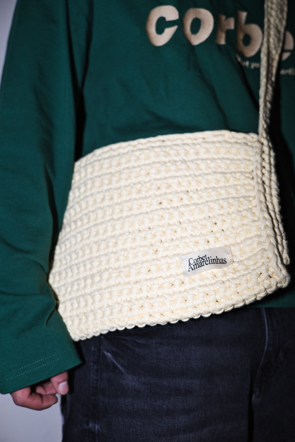 Yellow cream crochet crossbody bag with a wide strap, styled with a dark green streetwear long-sleeve with embroidered Corbet logo