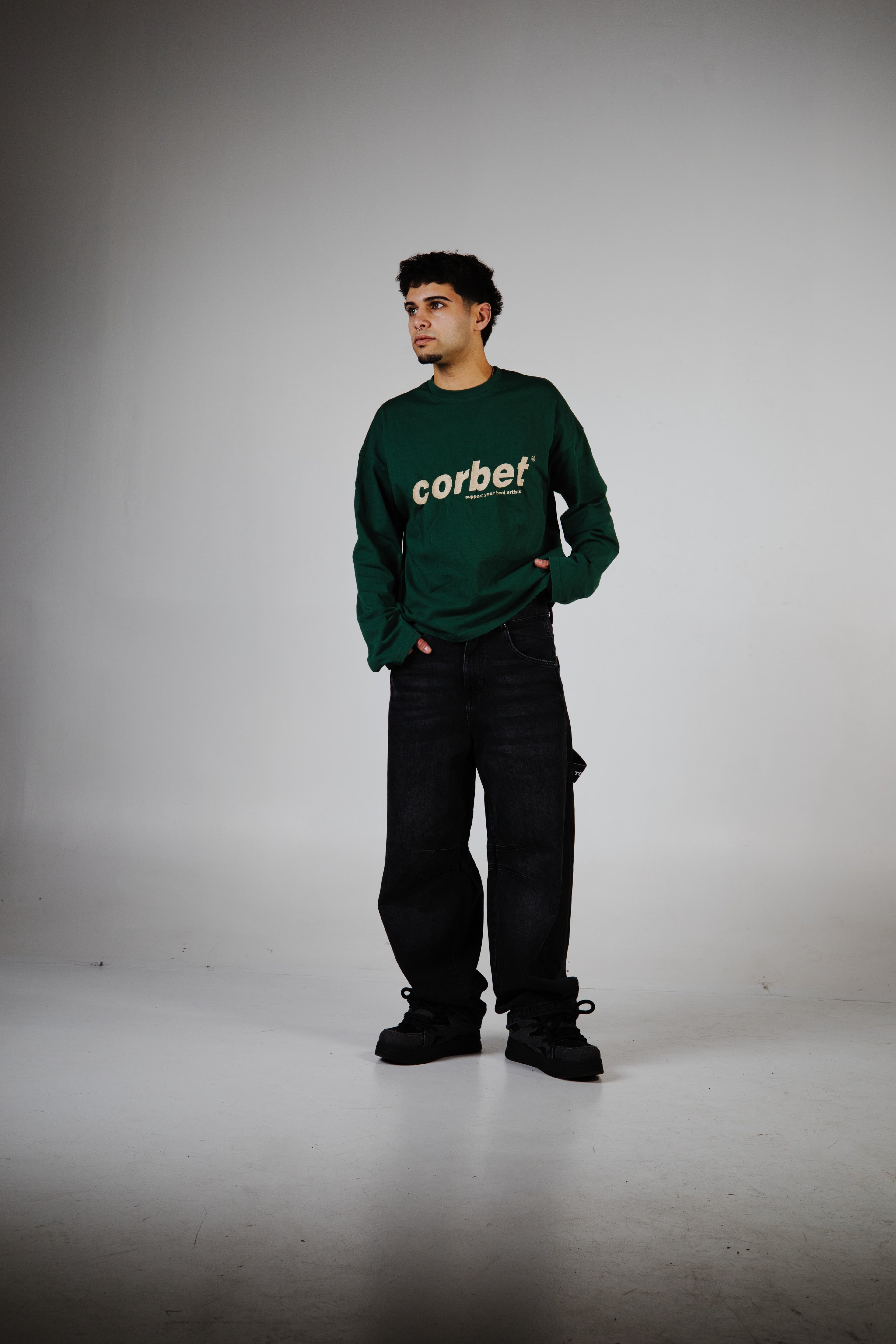 Person wearing a green longsleeveshirt with 'corbet' embroidered logo on a plain background