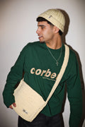 Model styling a matching crochet beanie and crossbody bag with a green long sleeve with embroidered logo