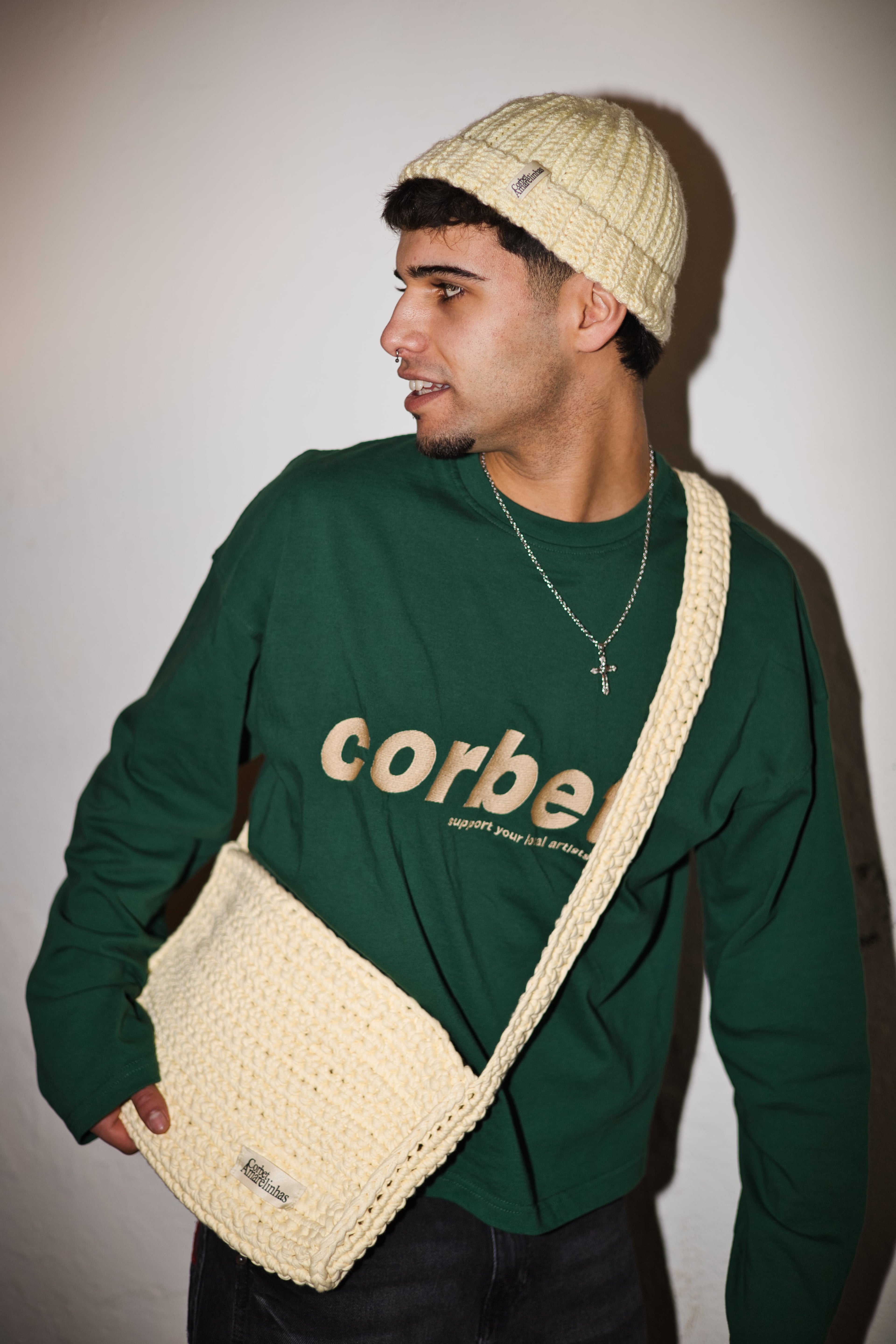 Model styling a matching crochet beanie and crossbody bag with a green long sleeve with embroidered logo