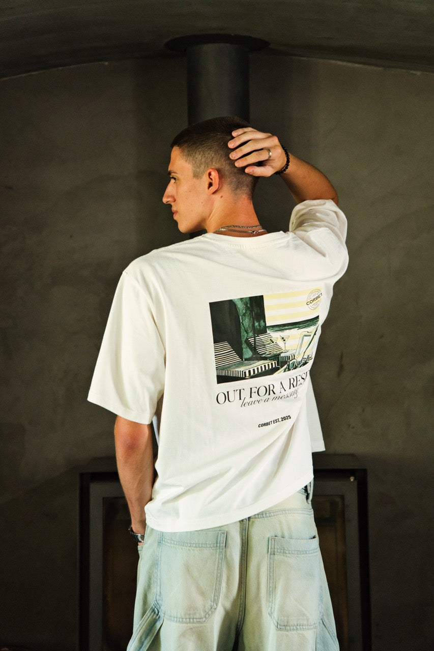 Man wearing a white t-shirt with a graphic design and text, standing against a dark background.