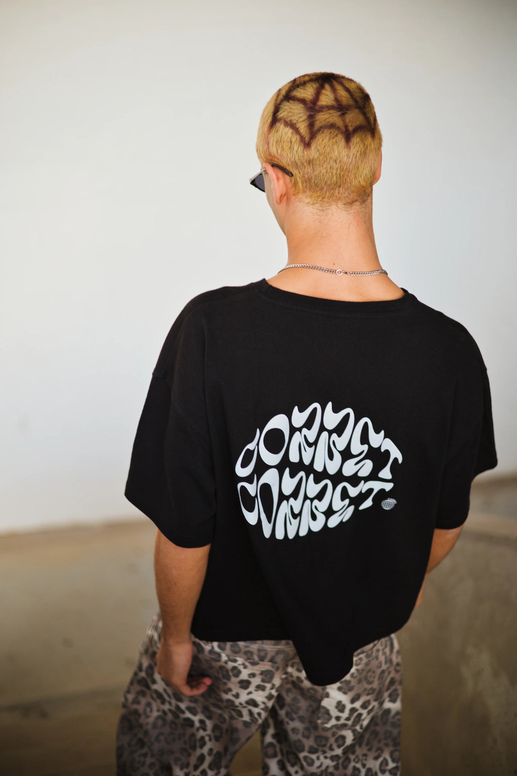 Person wearing a black t-shirt with white text on the back, standing against a plain background.