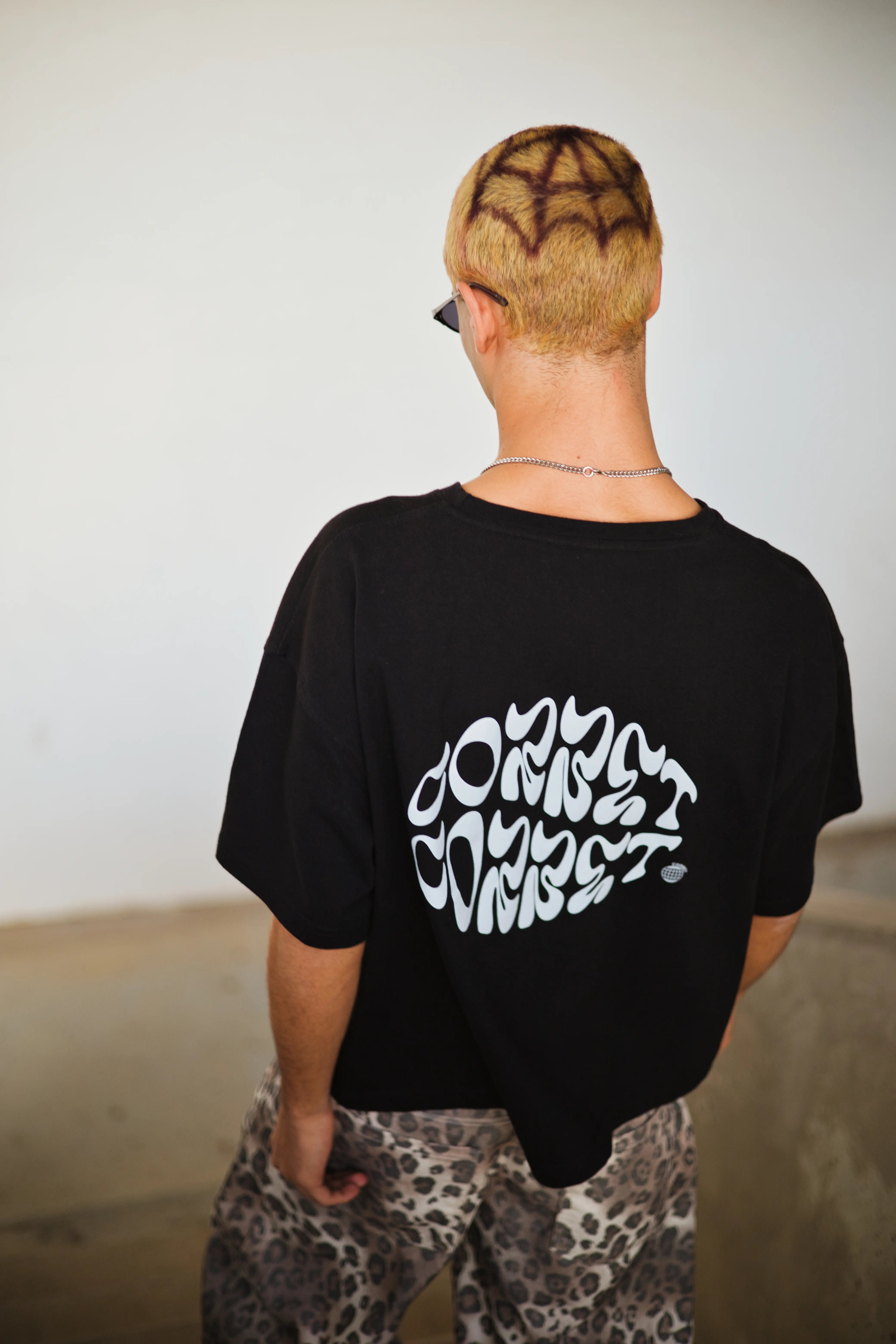 Person wearing a black t-shirt with white text on the back, standing against a plain background.