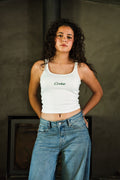 Woman wearing a white tank top and blue jeans against a dark background