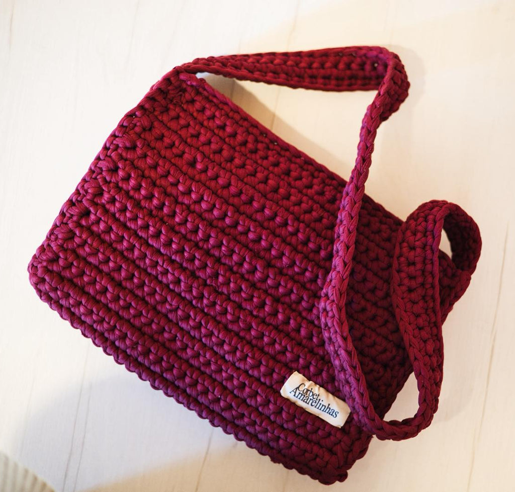 Maroon knitted crochet bag with a visible Corbet label on a light wooden surface.
