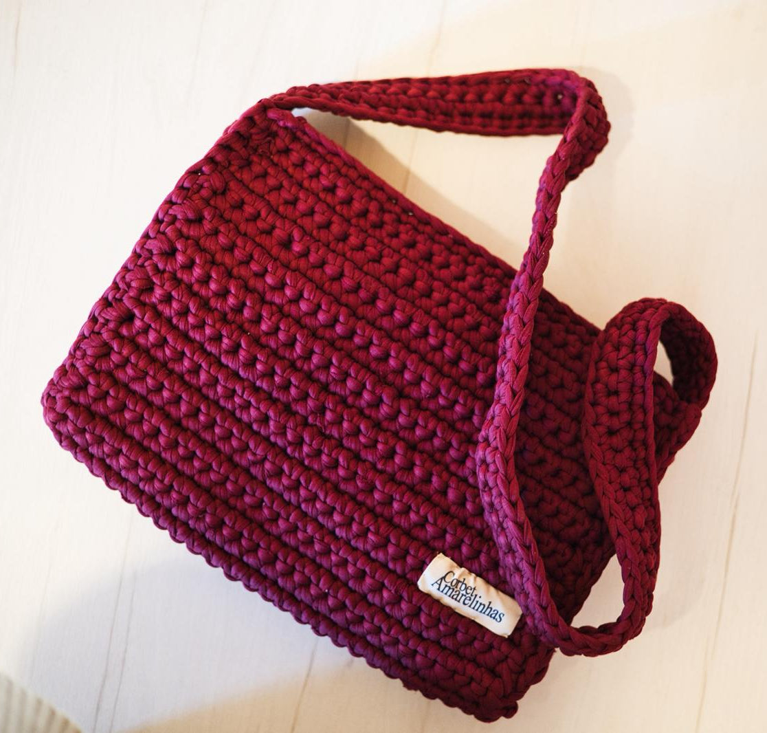 Maroon knitted crochet bag with a visible Corbet label on a light wooden surface.